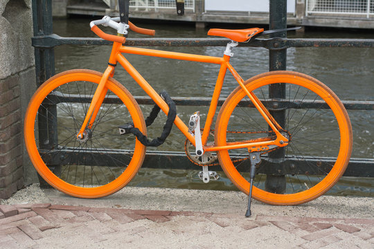 Orange bike is standing on pavement near the canal in Amsterdam