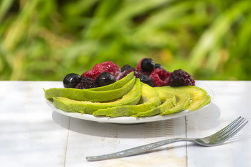 Healthy breakfast ingredients avocado slices with mix berries and honey.