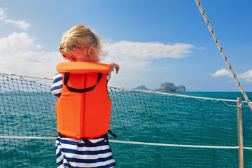 Happy little baby in life jacket on board of sailing boat watching offshore sea and tropical...