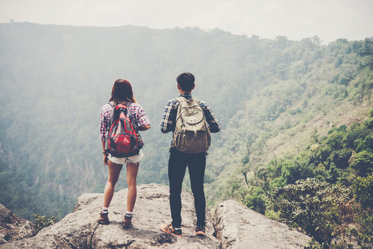 Hikers couple with backpacks standing on top of a mountain and enjoying nature view