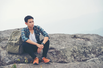 Young hipster Hiker with backpack sitting on top of the mountain.