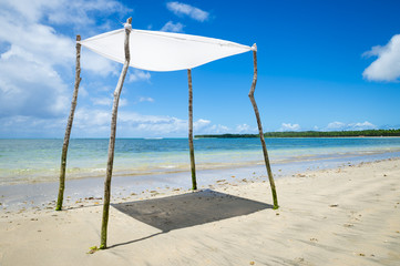 White sheet propped up by rustic sticks standing on bright Brazilian beach in remote Bahia, Brazil