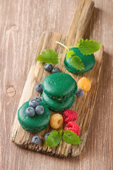 Traditional French sweets. A green makorunas with mint, white and red raspberries, blueberries on a wooden board. Dark background.