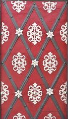 A very old red door with metal grey and white arabesques and diamonds; suitable to be used like background.