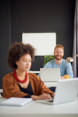 Young Caucasian businessman sitting and using laptop computer in modern office. In background colleague