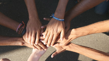 Arm of all races and colors stacked together one by one in unity and teamwork and then raised. Many multiracial hands getting together in the center of a circle and then cheer. Close up outdoor shot