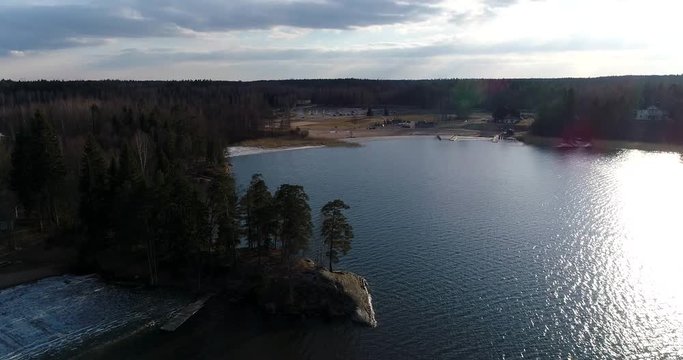 Oittaa, Cinema 4k aerial landing view behind trees at Oittaa beach, at bodom lake, on a sunny spring day, in Espoo, Finland