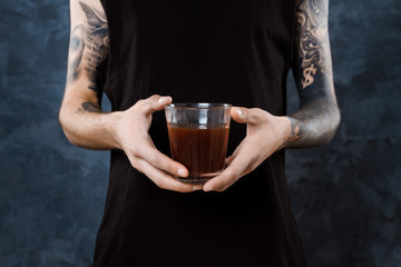 Male barista holding glass with coffee over grey background.