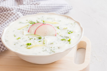 Yoghurt cold soup with radish, cucumber and dill on wooden board. Traditional soup tarator with radish and cucumber. Cold summer soup - okroshka. Healthy eating. Clean eating