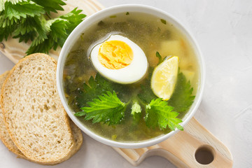 Nettle soup with vegetables and lemon in a white bowl on wooden board. Summer dishes. Light summer soup. Healthy vegetarian soup.
