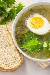 Nettle soup with vegetables and lemon in a white bowl on wooden board. Summer dishes. Light summer soup. Healthy vegetarian soup.