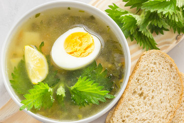 Nettle soup with vegetables and lemon in a white bowl on wooden board. Summer dishes. Light summer soup. Healthy vegetarian soup.