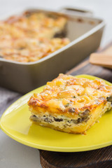 A piece of macaroni and cheese on a plate on wooden board. Baked pasta casserole in a ceramic baking dish.