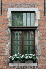 Fototapeta na wymiar Wooden window with flower pots in old brick building