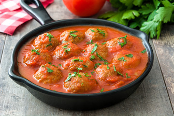Meatballs with tomato sauce in iron frying pan on wooden table