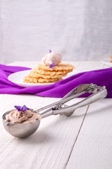 Spoon with ice cream. Belgian waffle on white plate decorated with purple flower.