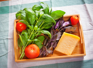 Green and purple basil, chunk of parmesan cheese and tomatoes on wooden tray