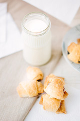 Home made croussants over fabric material with milk in bottle.