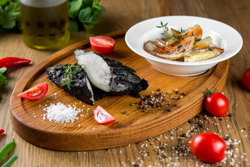 Charred chicken on a wooden board with potatoes.