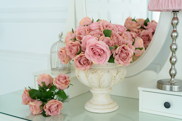 Bouquet of pink rores in vase on white boudoir table with oval mirror. Detail of the interior of the room with female boudoir