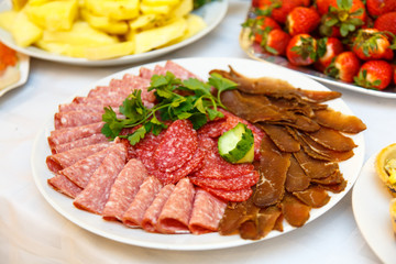 Slices of different sausages and meat lying on a plate on a festive table
