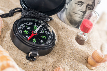 Fototapeta na wymiar sandglass, dollar and compass on sand isolated on white. summer concept