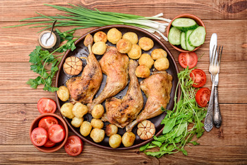 Chicken legs with baked potatoes and vegetables on wooden background.