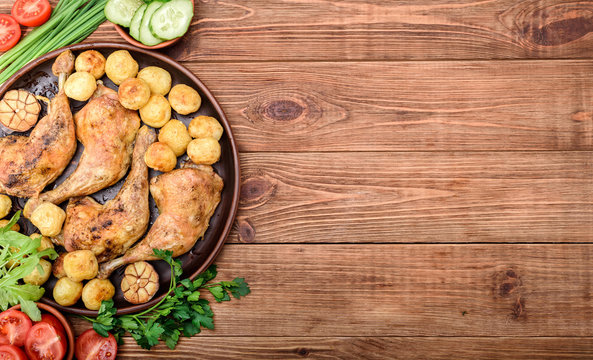 Chicken legs with baked potatoes and vegetables on wooden background.