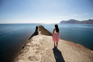 Girl in pink skirt walking at cape near sea in sunny weather