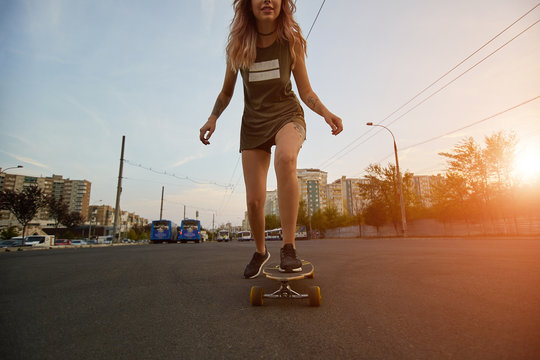 Beautiful young girl with tattoos riding on his longboard on the road in the city in sunny weather. Extreme sports