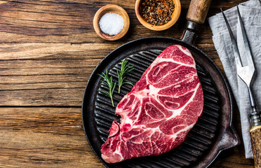 Raw beef marbled meat steak on vintage cast iron grill pan, spices and carving meat set on wooden rustic background. Top view