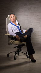 Business woman dressed into pants, white blouse, tie posing next to an office chair