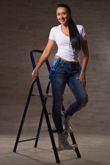Pretty adult woman dressed in jeans, a white T-shirt leans on a stepladder