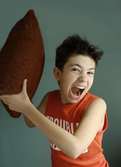 teenager mischivous boy fighting with pillow open mouth close up portrait