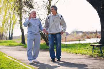Adult son walking with his senior father in the park.