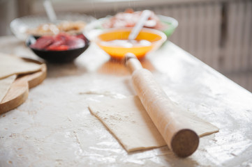 On the table the flour of the hand of the cook roll out the dough, the ingredients.