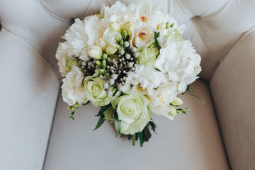 A bridal bouquet of flowers and greens stands on a white armchair