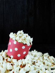 Popcorn in a red paper cup on a black background. Empty space for a text