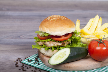 Delicious homemade chicken burger with fries, lettuce, tomato and cucumber on a wooden background