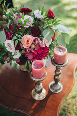 On the green grass there is a wooden table on which there is a composition of flowers and greens, and candles