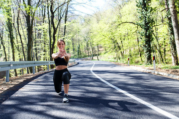 Young sports woman stretching his muscles before running in the woods on the road.