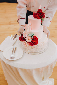 The waiter puts on a table a three-level wedding cake decorated with white and red flowers
