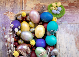 On the old wooden shabby table a dish of metal with painted in different colors Easter eggs with feathers willow and chickens