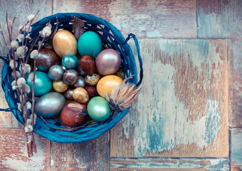 On the old wooden shabby table a dish with painted in different colors Easter eggs with feathers willow