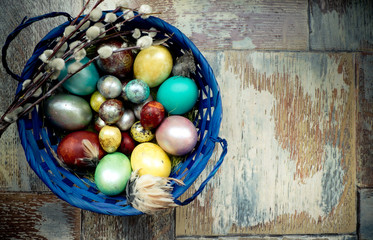 On the old wooden shabby table a dish with painted in different colors Easter eggs with feathers willow