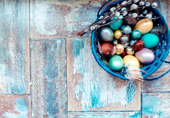 On the old wooden shabby table a dish with painted in different colors Easter eggs with feathers willow
