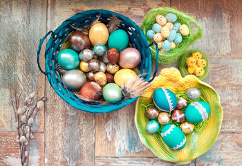 On the old wooden shabby table a dish with painted in different colors Easter eggs with feathers willow