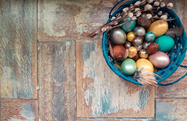 On the old wooden shabby table a dish with painted in different colors Easter eggs with feathers willow