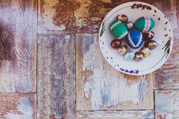 on the old wooden table is a plate of colored Easter eggs of quail and chicken with colored laces, and willow