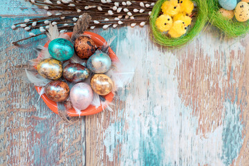 on the old wooden table is a plate of colored Easter eggs of quail and chicken with colored laces, and willow